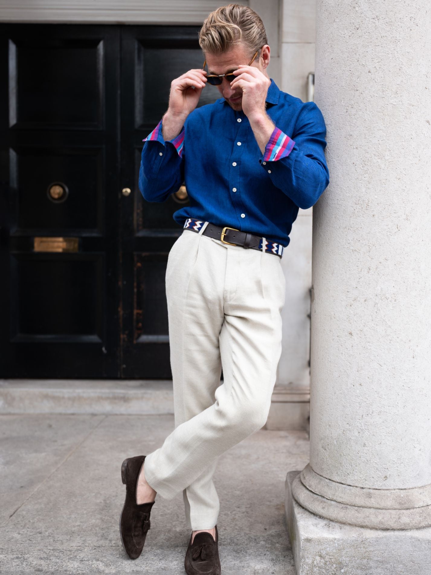 Man in a blue shirt and white pants standing against a columned building.